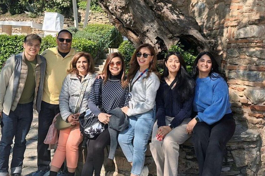 A group of people posing in front of a stone structure with greenery in the background. 4