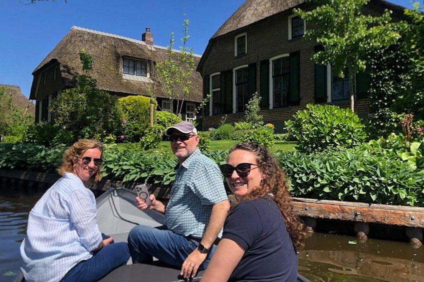 Tres personas en un bote en un canal, con casas al fondo. 3