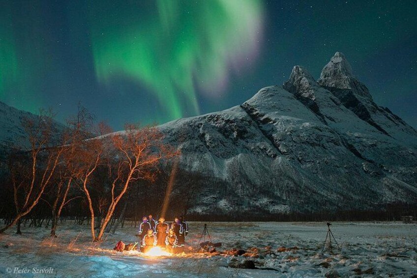 A snowy landscape with a mountain, trees, and a group of people around a campfire. 2