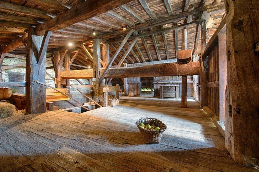 A rustic barn interior with wooden beams, a stone floor, and a basket of apples. 1