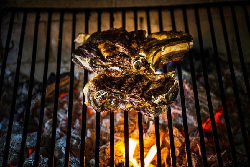 A grilled steak on a grill with visible grill marks and flames underneath. 2