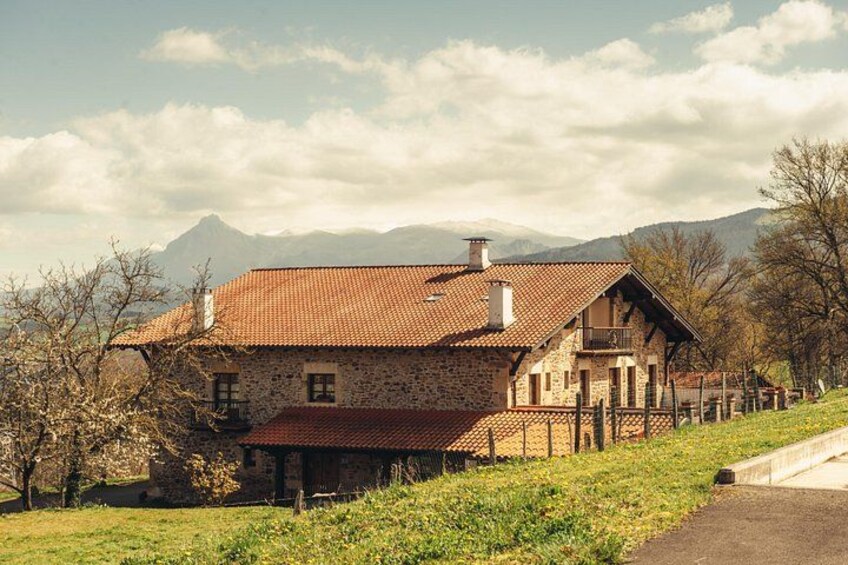 A stone house with a red-tiled roof, surrounded by a grassy landscape and trees, with mountains in the background. 4