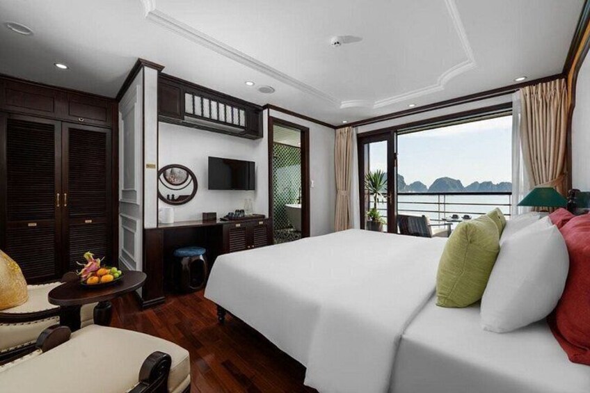 A modern hotel room with a large bed, a television, a desk with a chair, and a view of the sea. 5