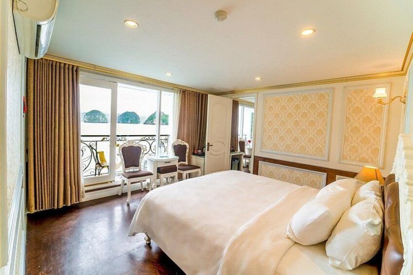A hotel room with a large bed, a balcony with chairs, and a view of the sea. 2