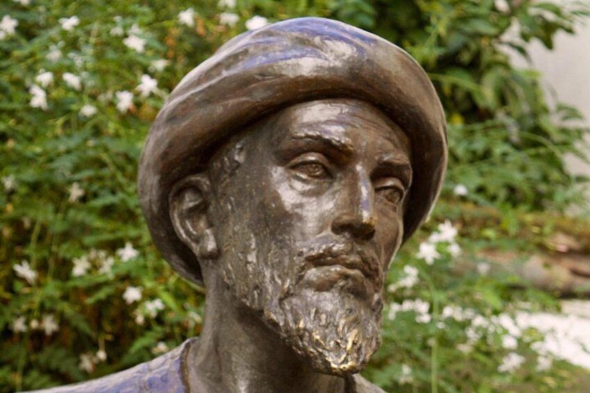 A statue with a hat, set against a backdrop of greenery and white flowers. 2
