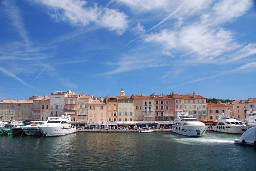 A marina with several yachts docked, a row of colorful buildings, and a clear blue sky. 3