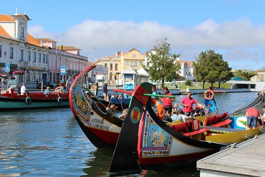 A traditional boat with passengers, docked at a pier with buildings in the background. 4