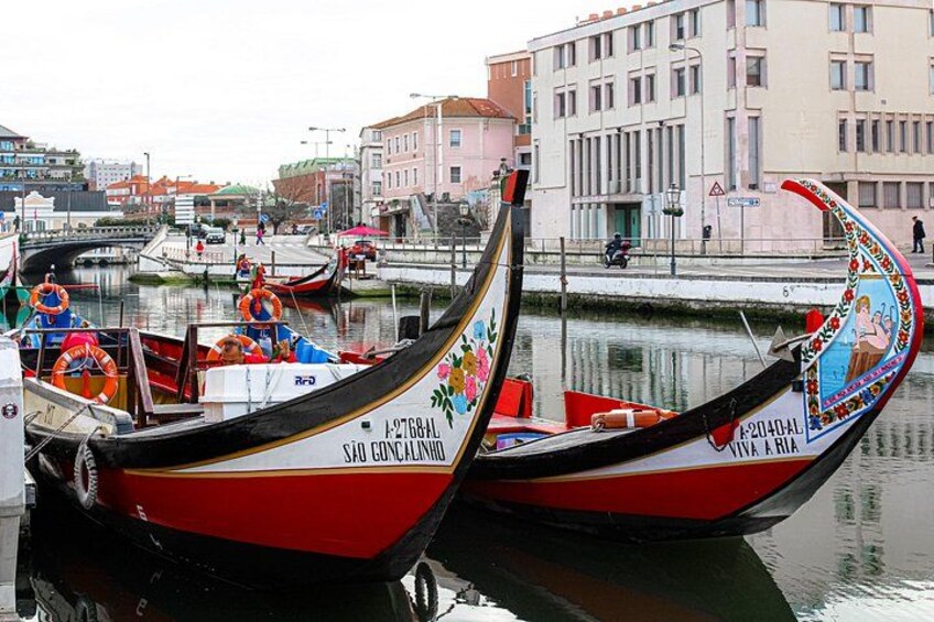 A row of traditional gondolas docked at a waterfront, with buildings and a pedestrian walkway in the background. 2