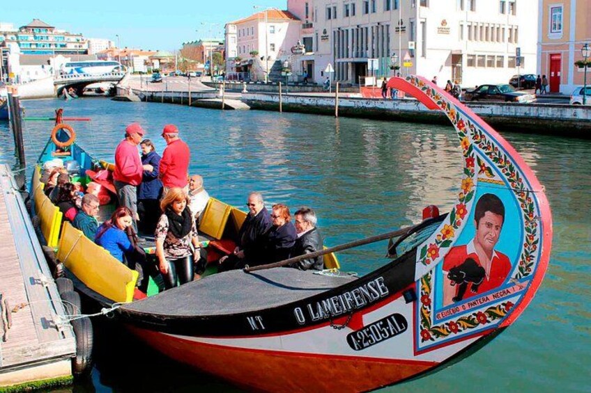 A colorful boat with people on board, docked at a marina with buildings in the background. 1