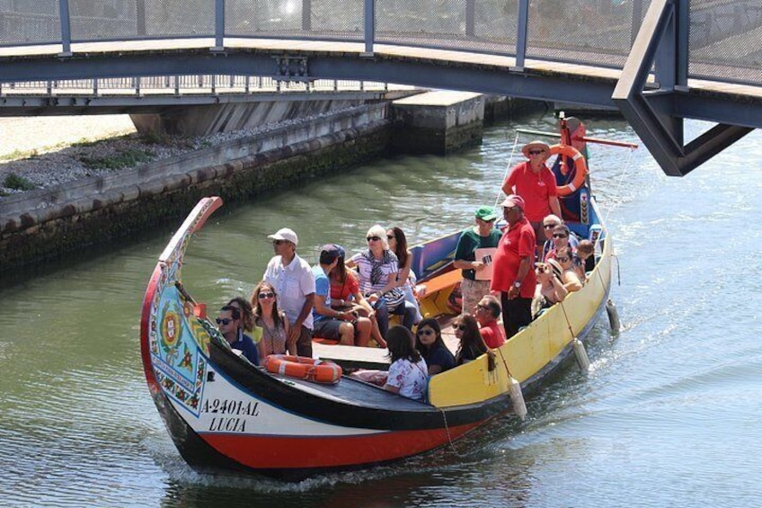 Ein farbiges Boot mit Passagieren, im Hintergrund eine Brücke und ruhiges Wasser. 5