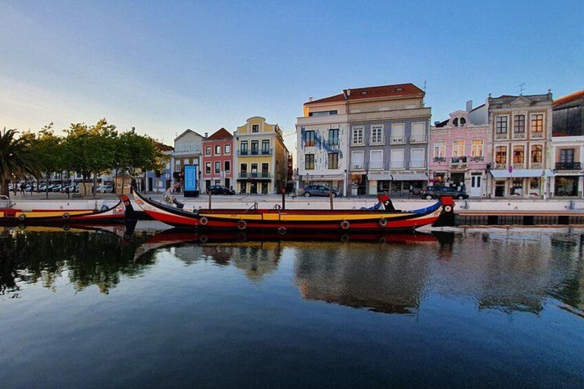 A calm river with two traditional boats docked, colorful buildings along the riverbank, and a clear sky. 3