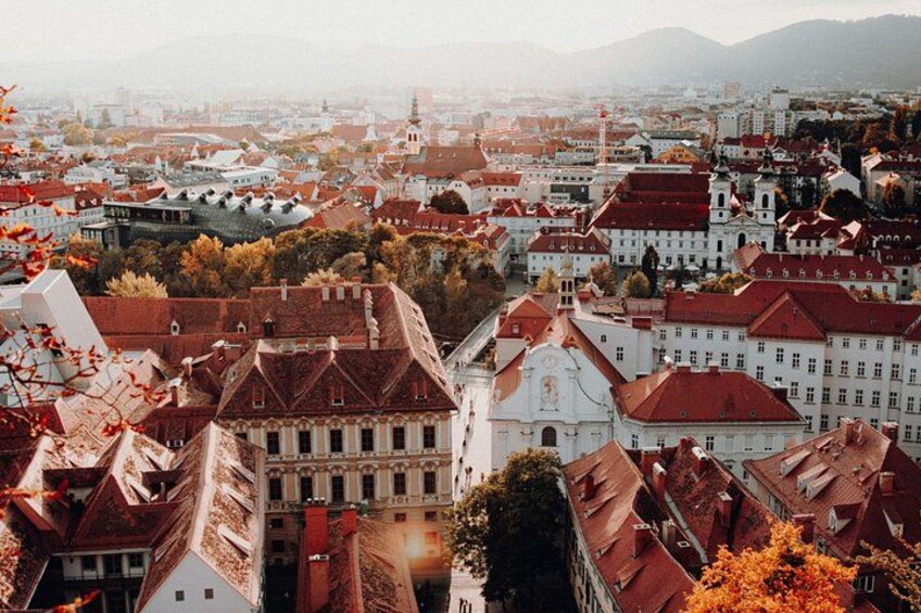 A cityscape with red-roofed buildings, a prominent white building with a dome, and autumn foliage. 4