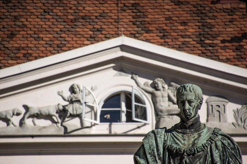 A statue in front of a building with a detailed facade, including a window and a brick roof. 5
