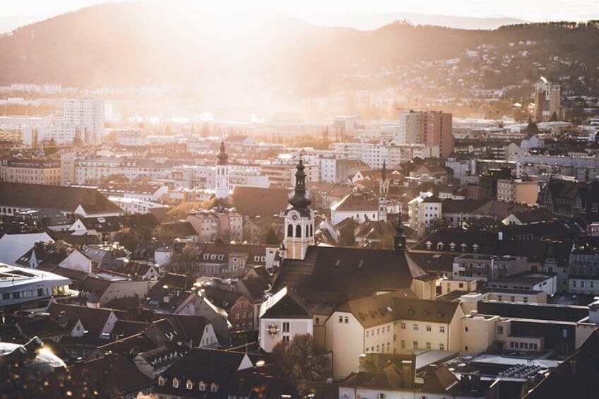 A cityscape with a prominent church tower, dense urban buildings, and a hilly backdrop. 2