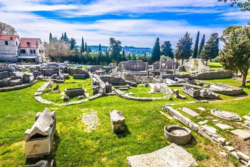 Ancient ruins with stone structures and pathways, surrounded by grass and trees. 3