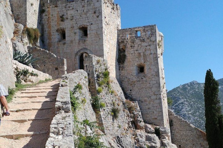 A stone staircase leading up to a medieval fortress with a clear sky. 1