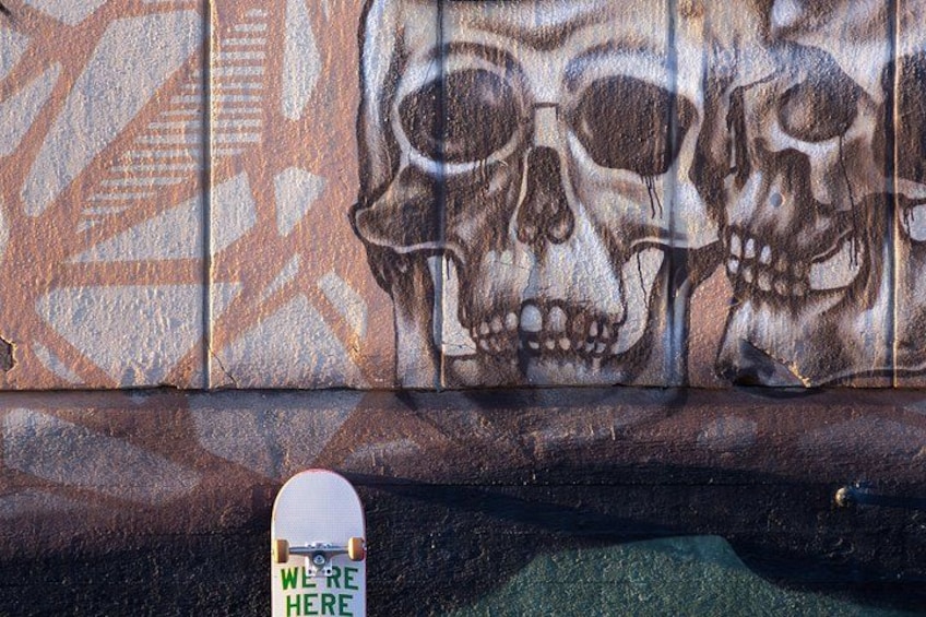 En væg med graffiti af kranier og et skateboard med klistermærke. 5