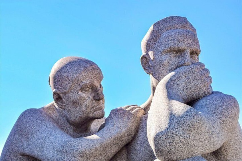 Two large stone statues with arms crossed, set against a clear blue sky. 2