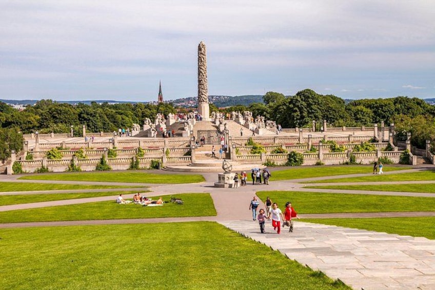 Un parque grande y abierto con un monumento alto, senderos y una estructura que parece un castillo al fondo. 2