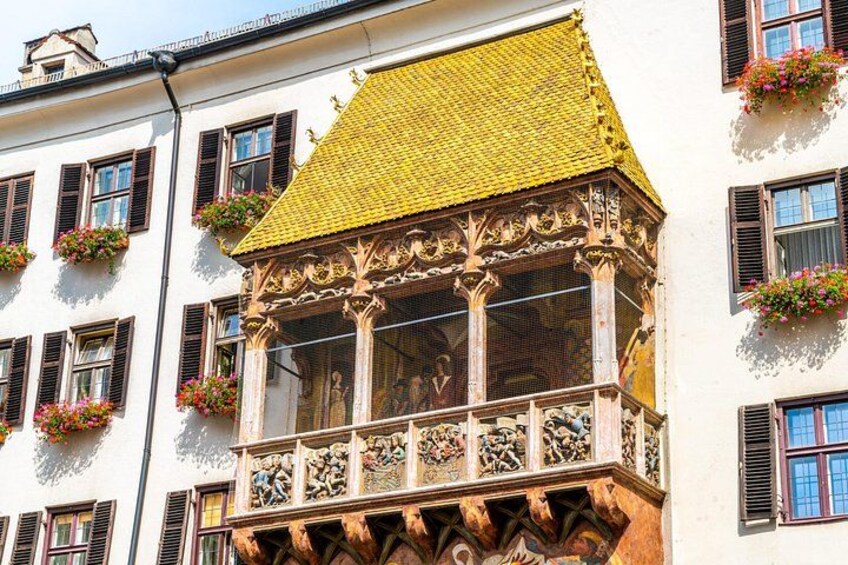 A building with a yellow tiled roof, ornate balcony, and flower boxes. 1