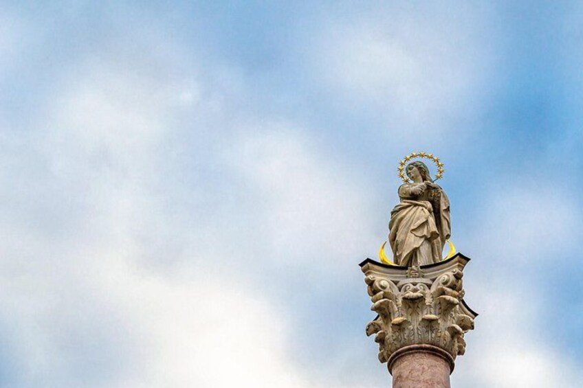 A statue on a column with a halo, set against a cloudy sky. 3