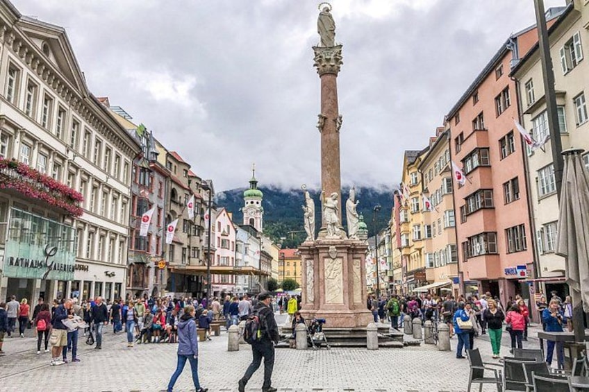 A crowded square with a central monument, surrounded by historic buildings and a mountain in the background. 3
