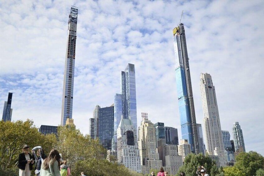 A cityscape with modern skyscrapers, a park with people, and a partly cloudy sky. 1