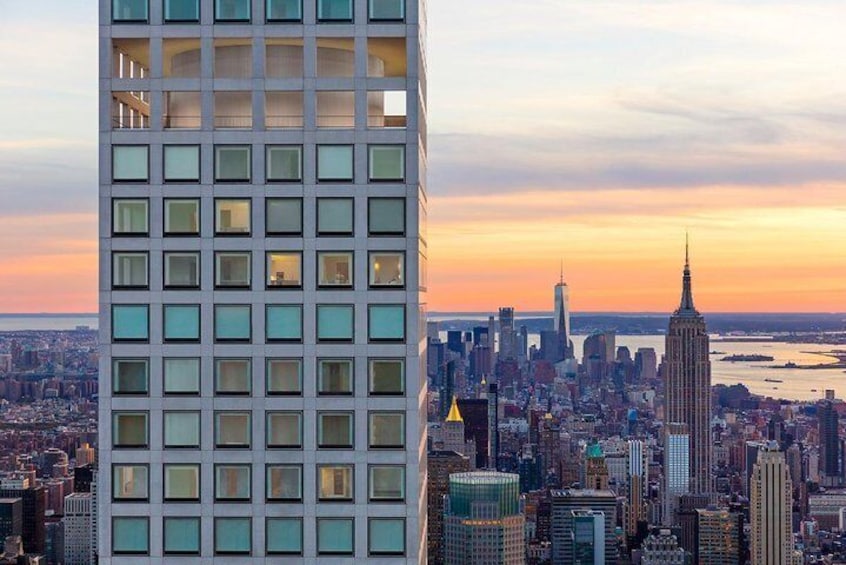 A cityscape with a prominent building in the foreground and the Empire State Building in the background. 2