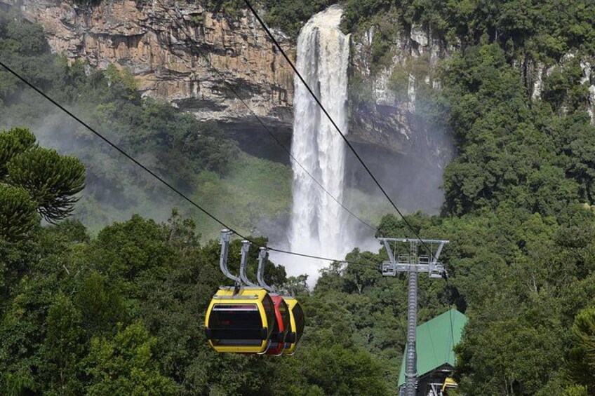 A cable car suspended above a waterfall, surrounded by dense forest. 2