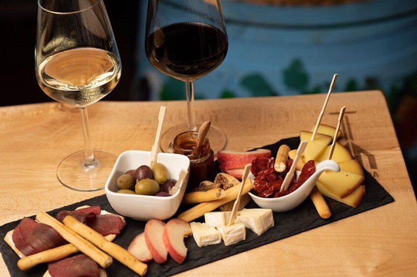En skænkebakke med forskellige oste, pålæg og frugter, samt glas vin. 5