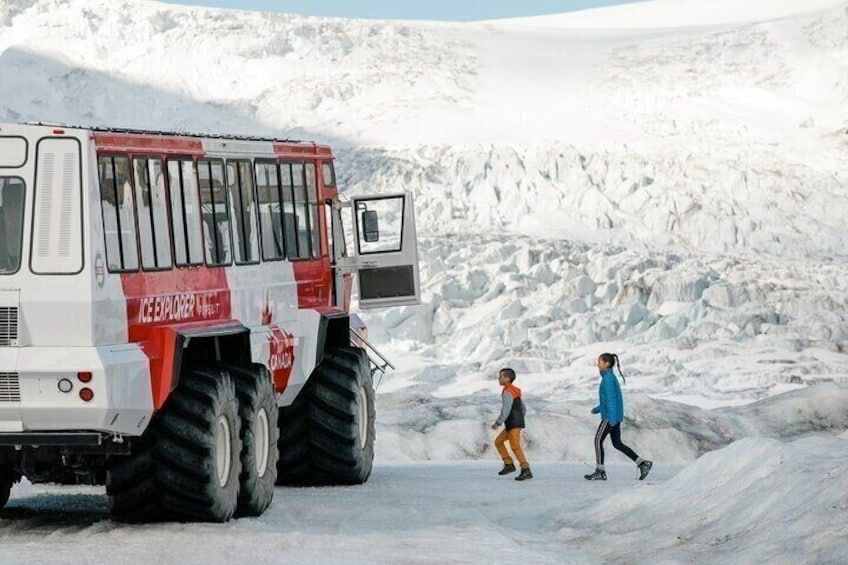 Ein großes Fahrzeug mit der Aufschrift 'Ice Explorer', eine verschneite Landschaft und zwei Personen beim Gehen. 4