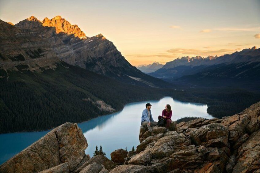 Eine Berglandschaft mit einem See, felsigem Gelände und zwei Personen, die auf einem Felsen sitzen. 1