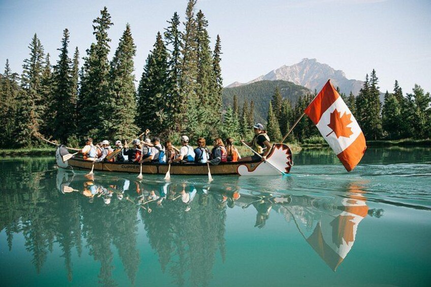 Ein Kanu mit paddelnden Personen auf einem ruhigen See, umgeben von Bäumen und Bergen. 5