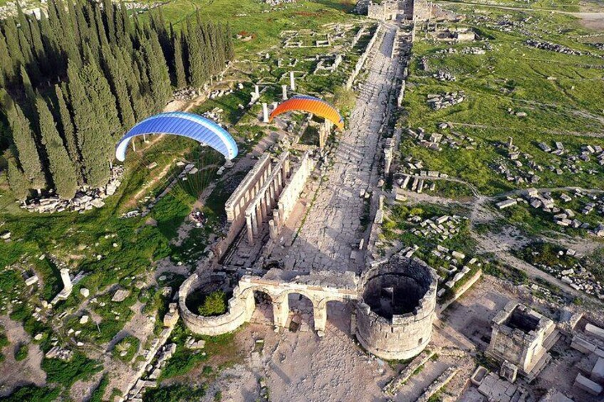An ancient city with ruins, a large circular structure, and a modern glass bridge. 2