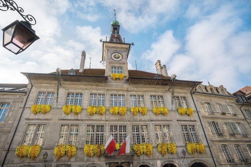Een historisch gebouw met een klokkentoren, gele bloemen en vlaggen. 3