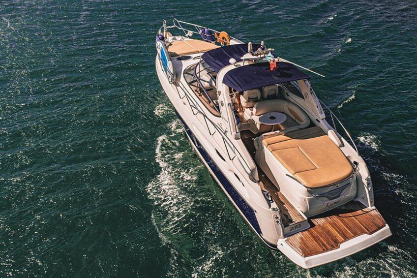 A large motorboat with a wooden deck and a covered seating area, moving through the water. 3