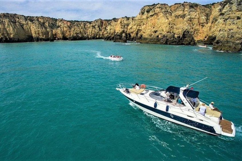 A yacht on turquoise water with rocky cliffs in the background. 1