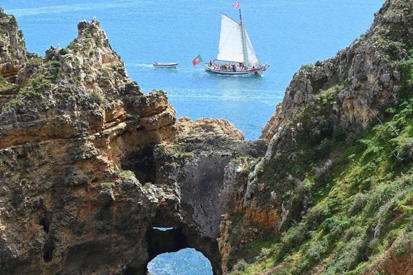 Un paisaje costero con acantilados rocosos, un estrecho canal de agua y un velero con una bandera. 4