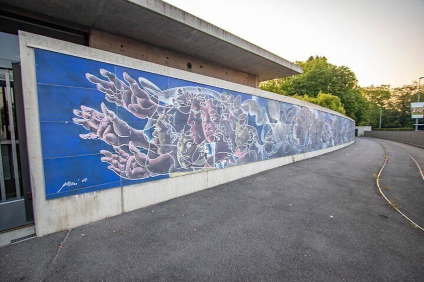 Un murale su un muro di un edificio, una strada curva e un albero sullo sfondo. 2