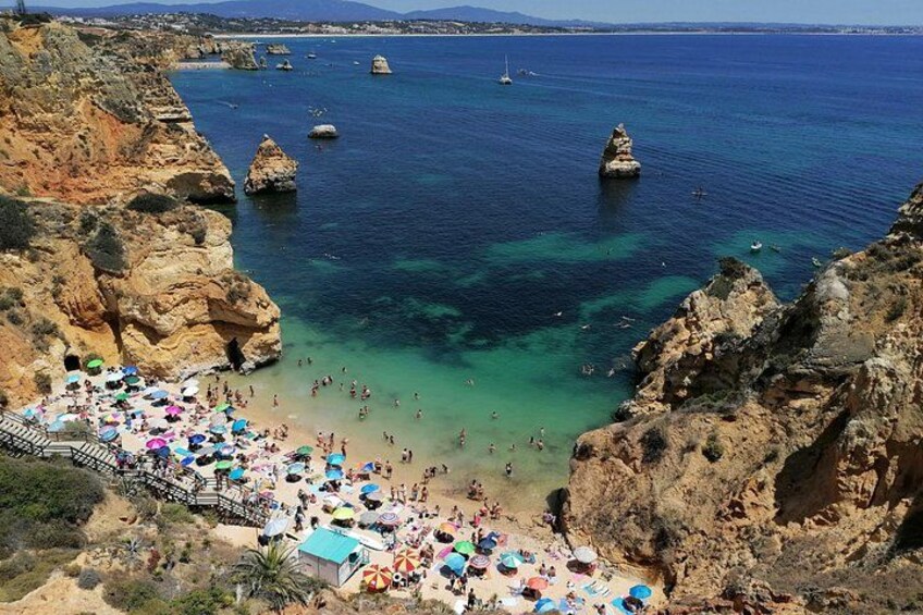 Una playa costera con agua azul cristalina, acantilados rocosos y numerosos sombrillas. 1