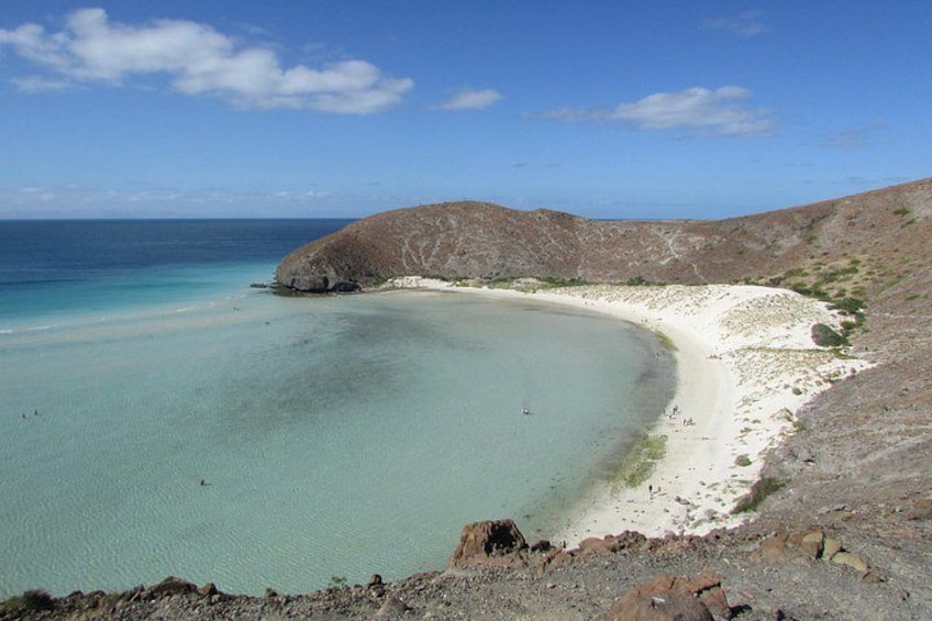 A coastal landscape with a sandy beach, clear turquoise waters, and a rocky hill in the background. 2