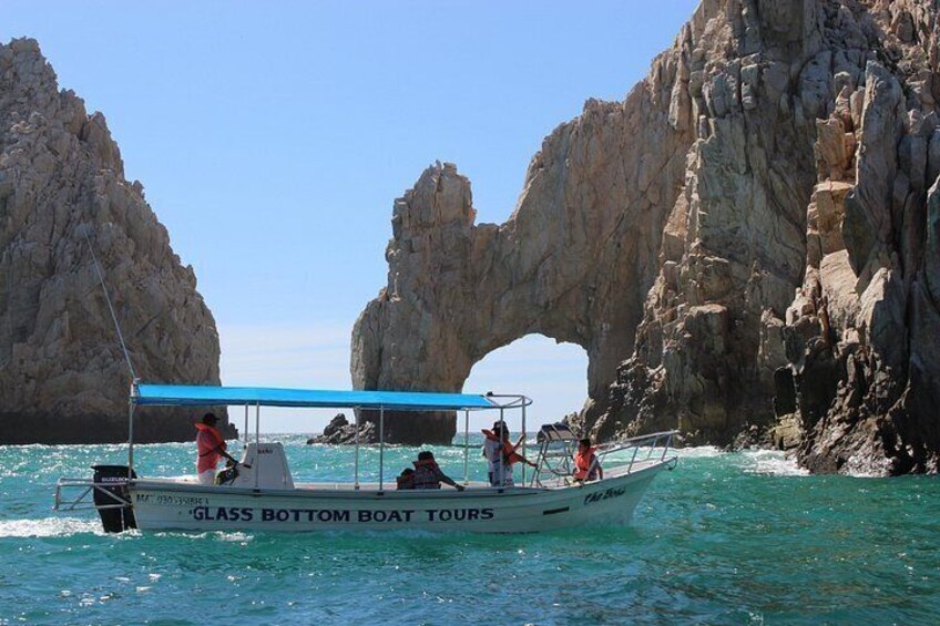 A boat tour named 'GLASS BOTTOM BOAT TOURS' navigating through a clear blue sea with rocky cliffs and an arch formation in the background. 2