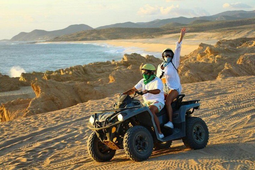 Two people on an ATV in a desert with a beach and mountains in the background. 2