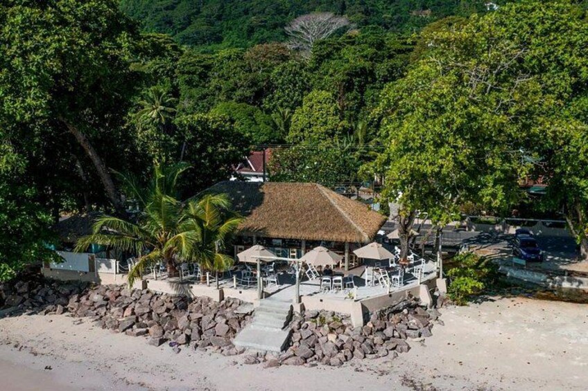 A beachside resort with a thatched-roof building, palm trees, and a rocky shoreline. 2