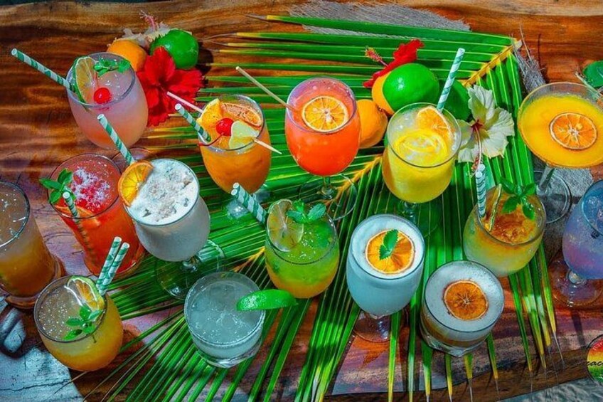 A variety of colorful cocktails arranged on a wooden surface with tropical decorations. 3