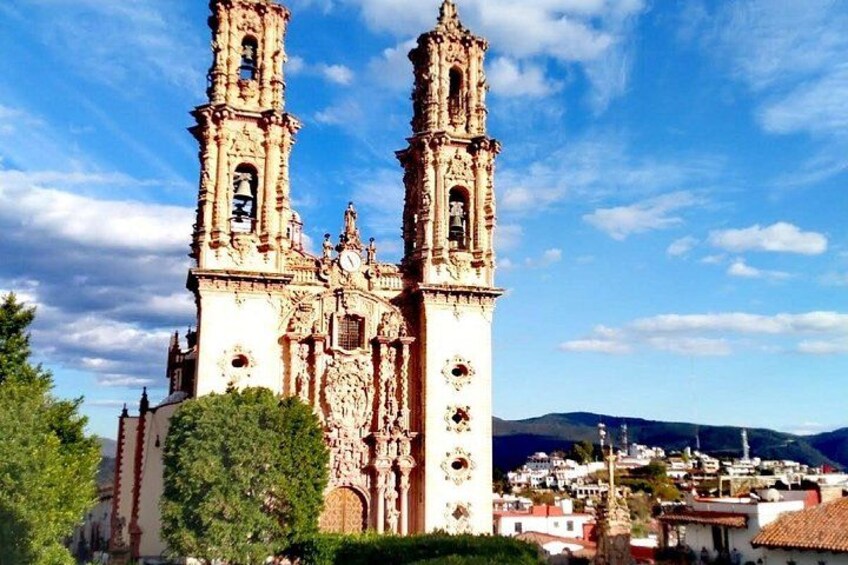 A historic church with two bell towers, surrounded by greenery and a mountainous backdrop. 1