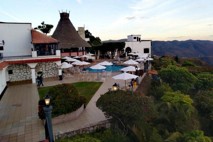 A poolside area with umbrellas and lounge chairs, surrounded by greenery and overlooking a mountainous landscape. 5