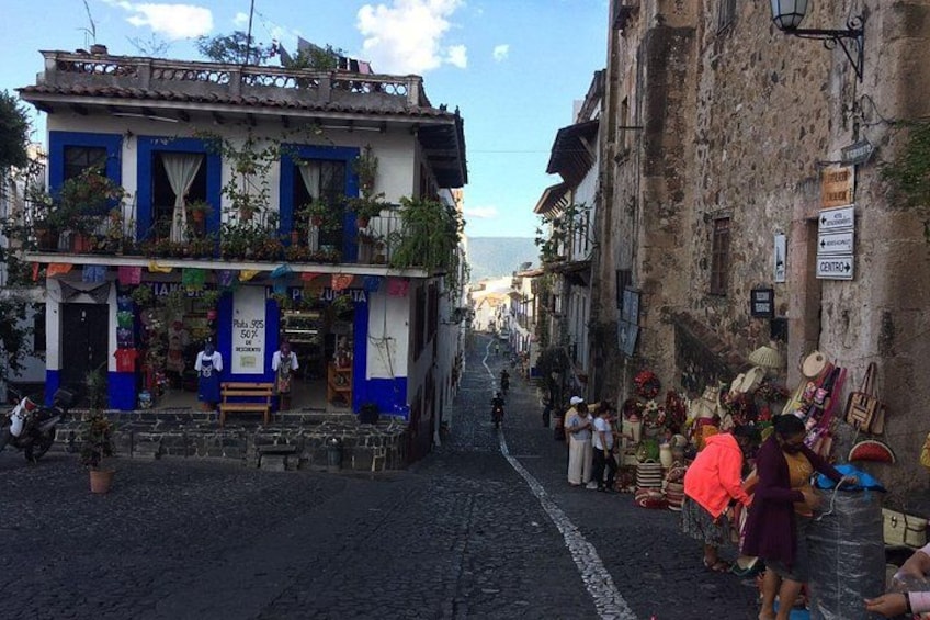 A cobblestone street with buildings, a shop with colorful decorations, and a sign indicating a central location. 2