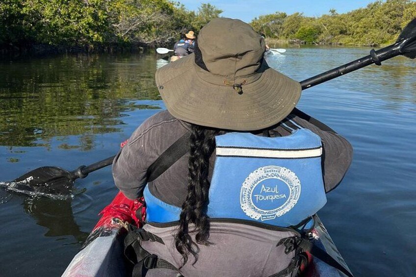 A person kayaking on a calm river, wearing a hat and a life jacket with 'Azul Turquesa' branding. 2