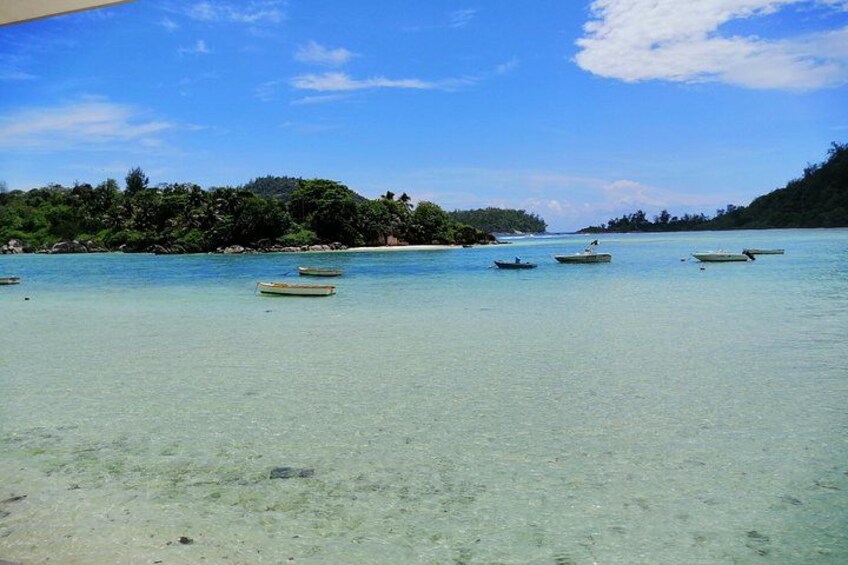 Ein klares türkisblaues Meer mit Booten, ein Sandstrand und eine bewaldete Insel im Hintergrund. 2